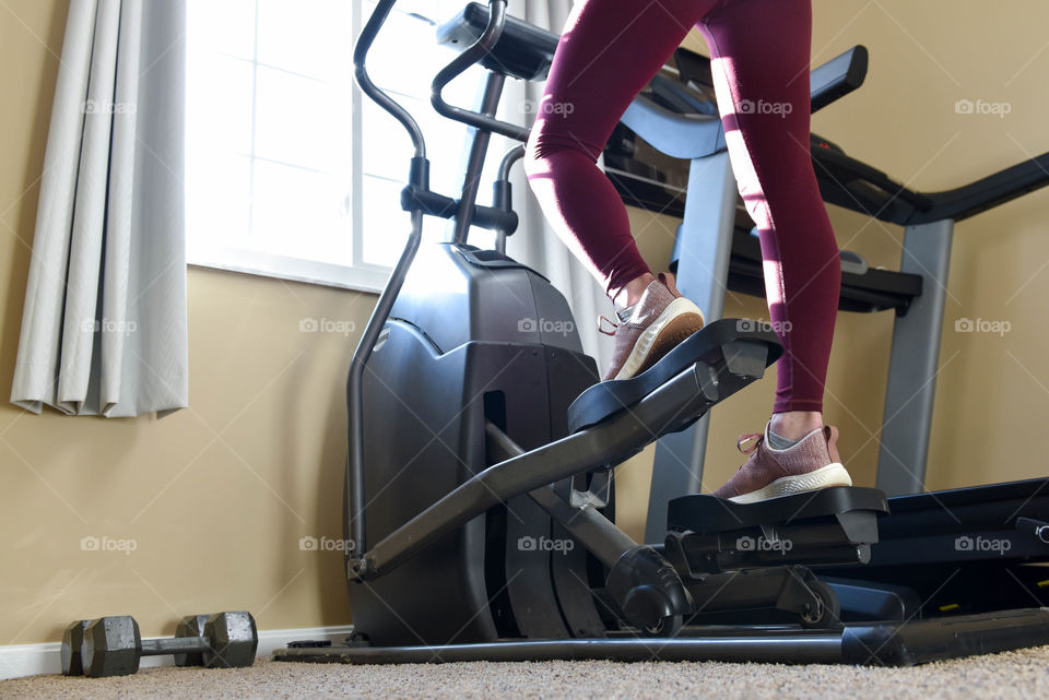 Bottom half of a woman shown using an elliptical machine in front of a bright window