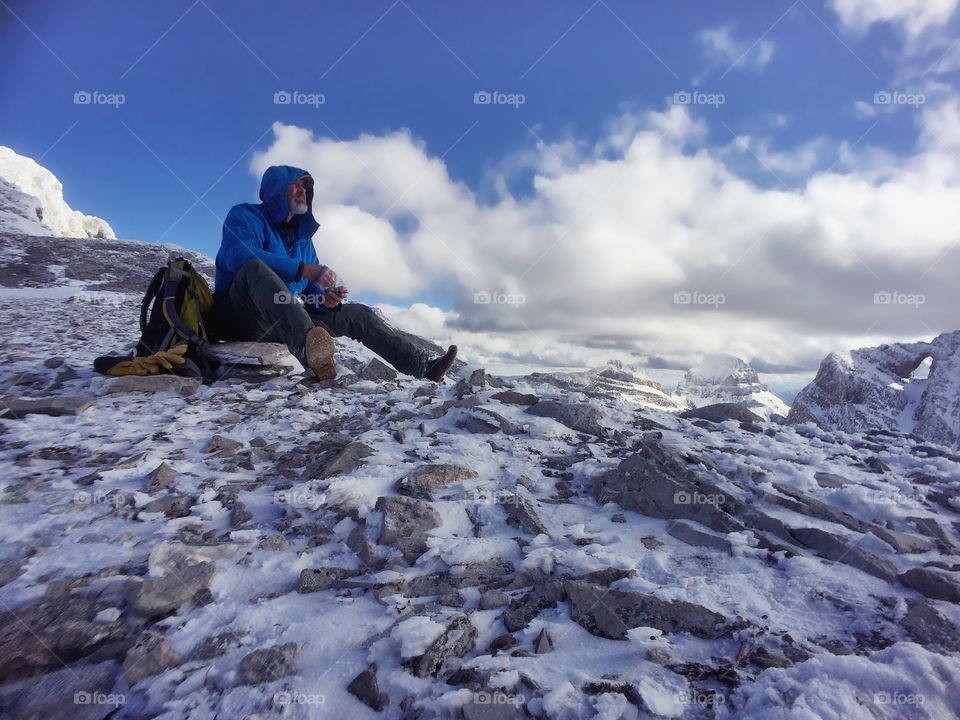 Senior man sitting on rock with backpack in winter