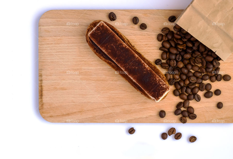 Eclair with cream near the coffee beans on the wooden board.