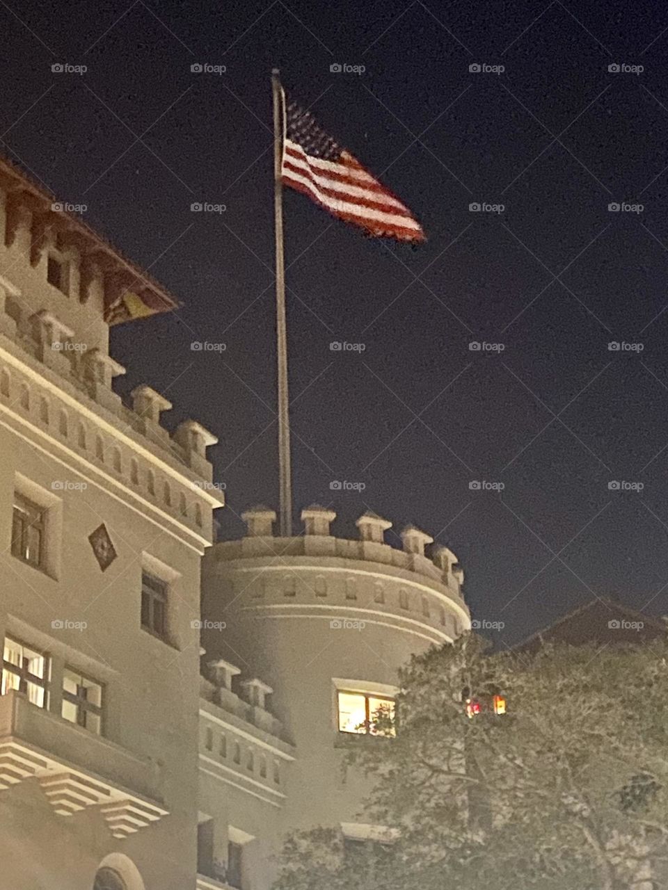 The top of a building that looks like a castle with an American flag flying on a pole above it against a dark night sky 