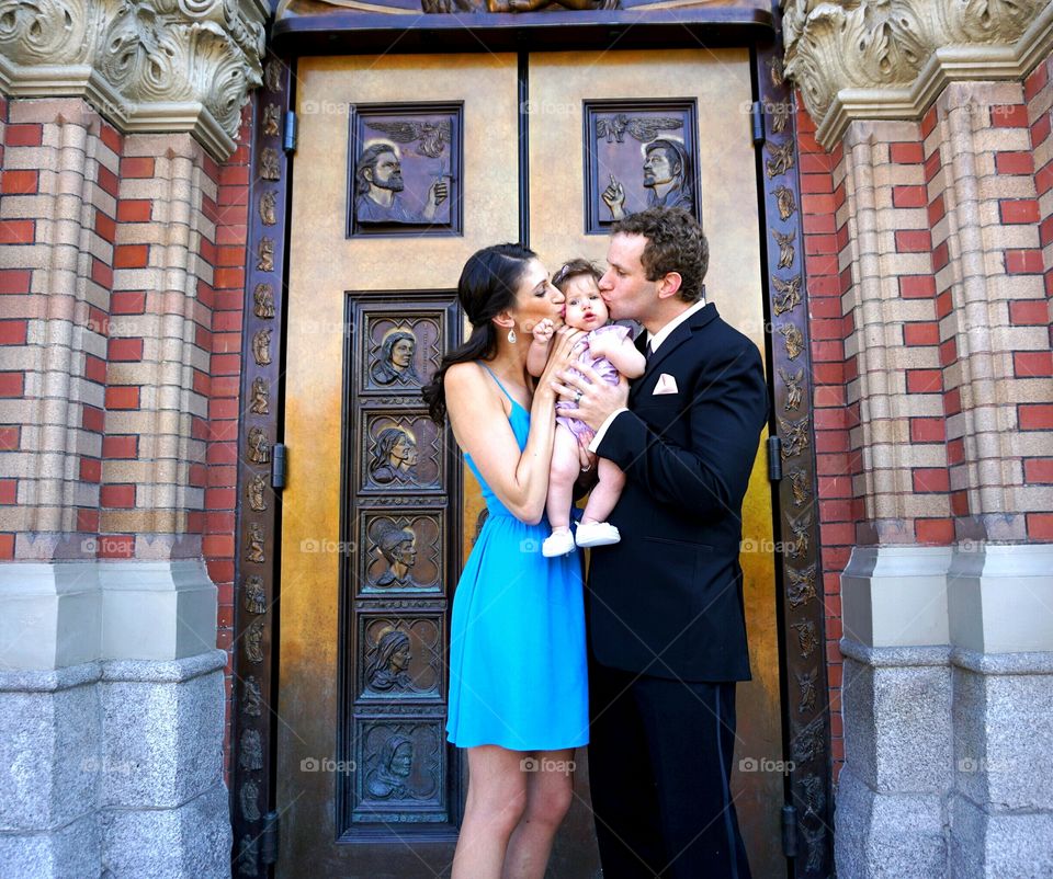 Mother and father kissing their daughter on her cheek
