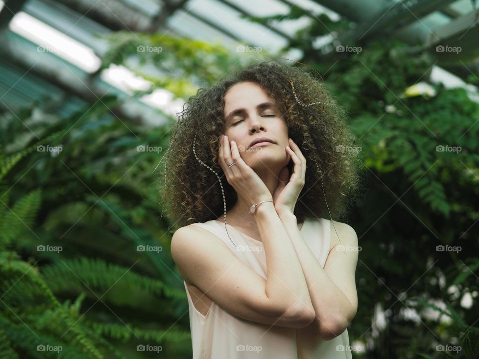 Portrait of beautiful curly woman with closed eyes in botanical garden, portrait of woman 