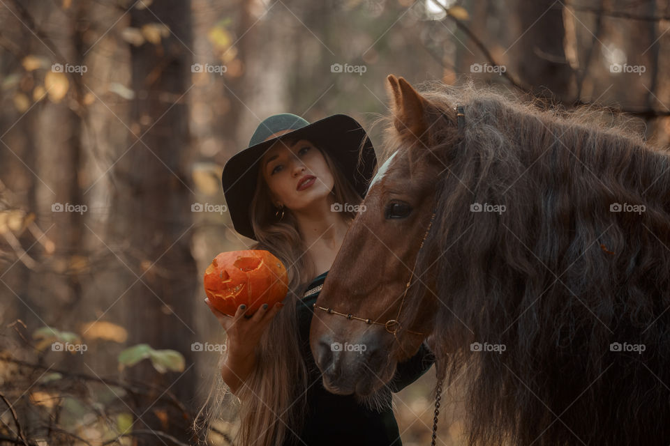 Woman in witch wear with horse in autumn park 