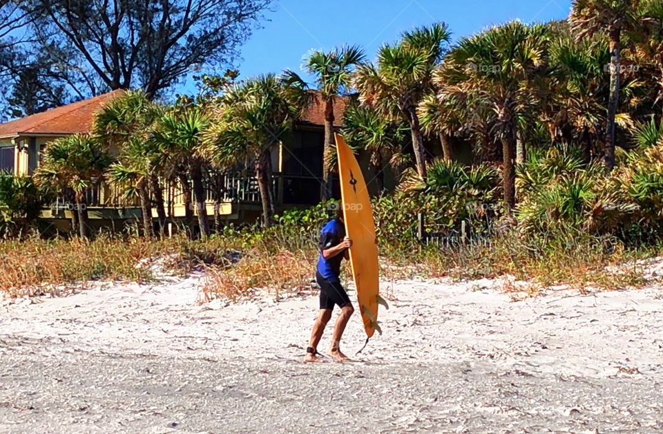 Young man on the beach with his favorite surf board preparing to ride the waves.