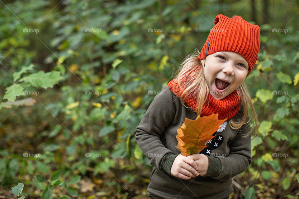 portrait smiling of a girl in an orange hat with an autumn leaf the background of nature