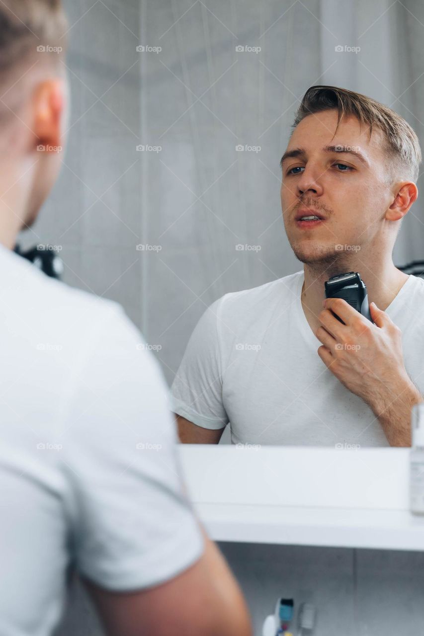 Man shaving his beard in bathroom using electric shaver 