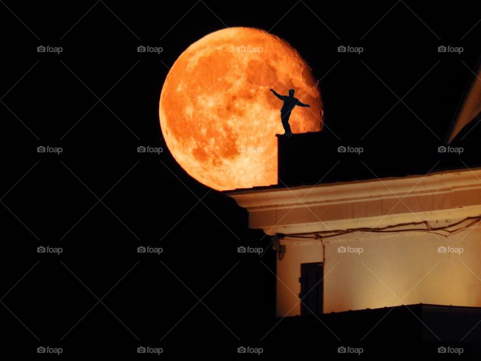 Big red moon over the roof with a silhouette of a man