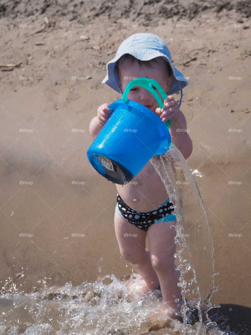 Toddler girl pouring water out of her bucket at the beach.