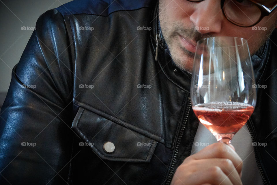 A man with a leather jacket and stubble sniffs a stemmed glass with Rosé wine in it.