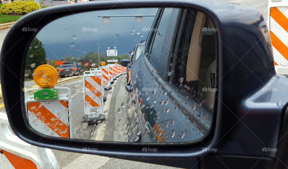 Road construction pylons line the highway during a commute. The view from the side view mirror gives a great perspective.