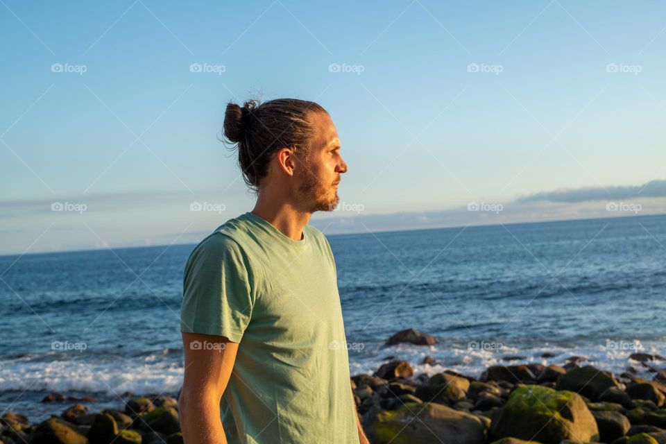 Man with much hair facing the sun at the sea