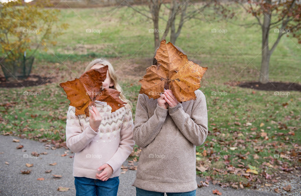 Two children each holding a large maple leaf in front of their faces