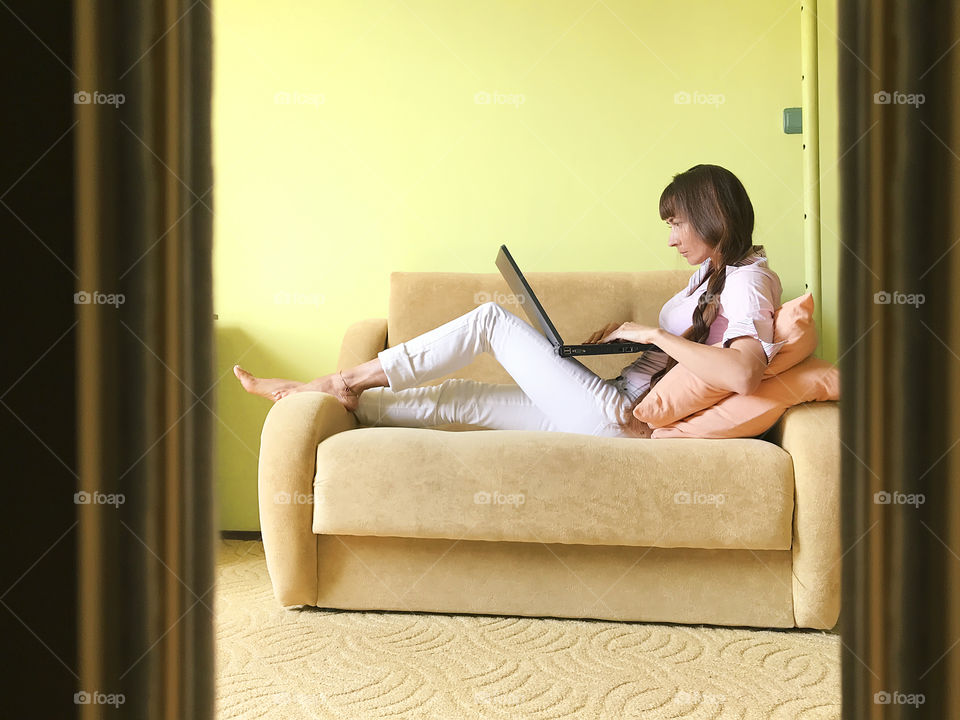 Young woman using her laptop on the favorite yellow sofa in the yellow living room at home 