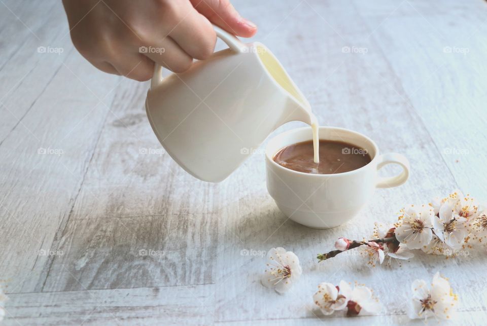 Person poring milk in the cup with coffee.