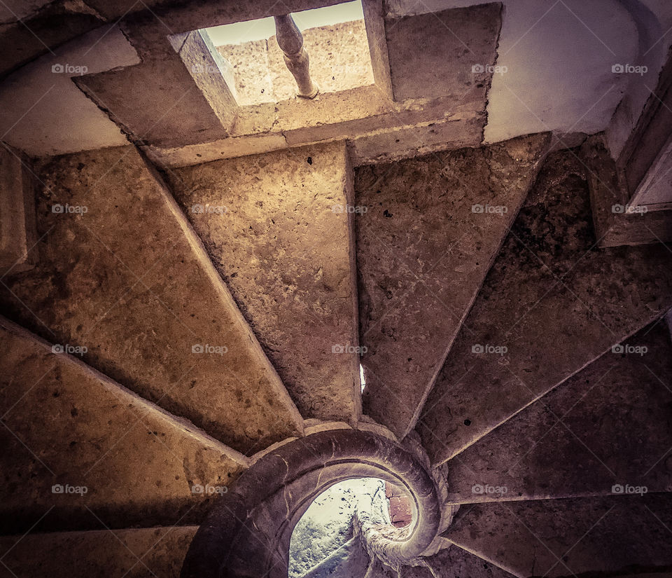 Looking downwards from the top of a stone, spiral staircase, gentle light comes in through a small window 