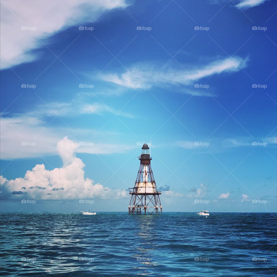 Boats anchored near a lighthouse under a partly cloudy blue sky