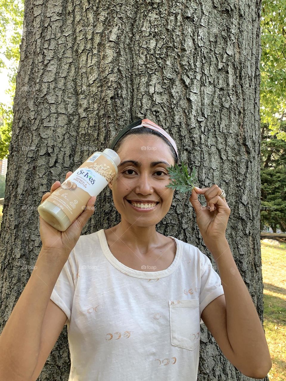 Energetic person holding St. Ives oatmeal shea butter soothing body wash against a big tree. 