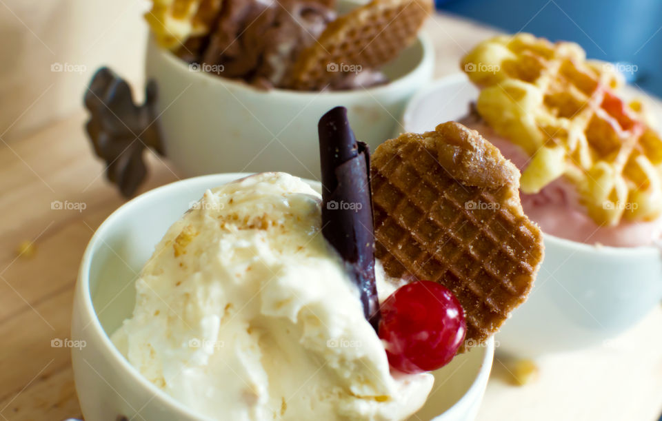 Vanilla ice cream scoops in bowl topped with chocolate and maraschino cherry and Netherlands Dutch syrup caramel waffle "stroopwafel" with strawberry ice cream and chocolate ice cream in background with bitesize Belgian waffles 