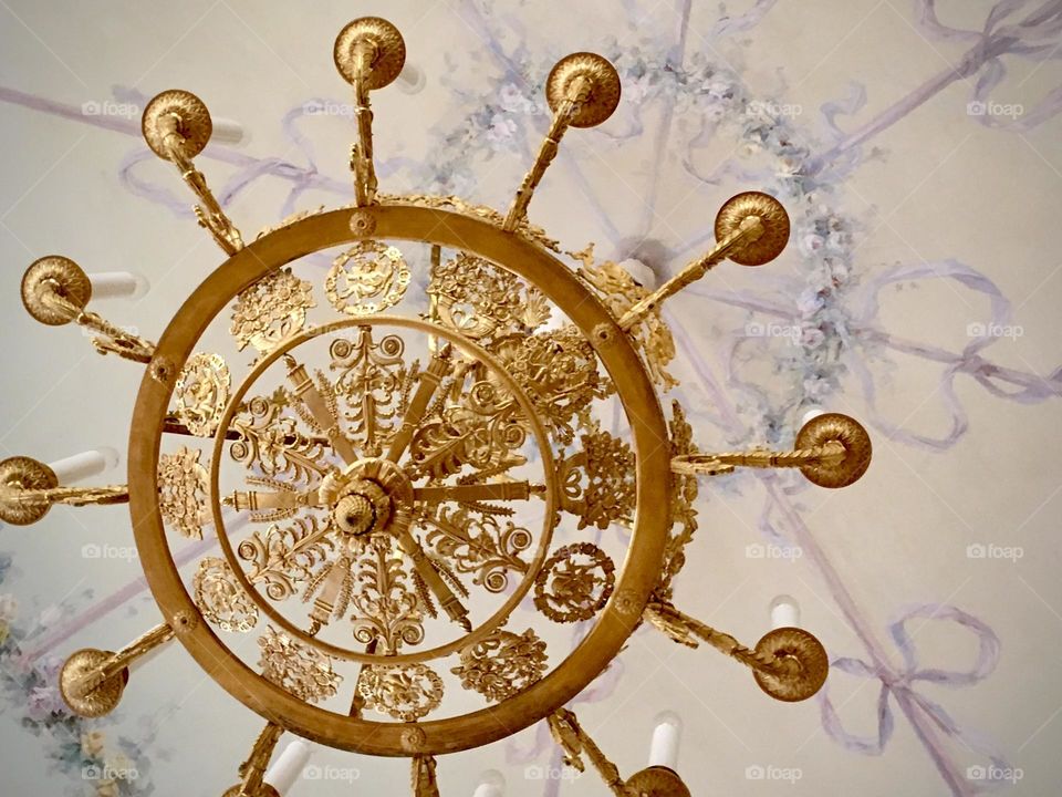 An ornate gold chandelier is pictured from below, showcasing the white marble ceiling