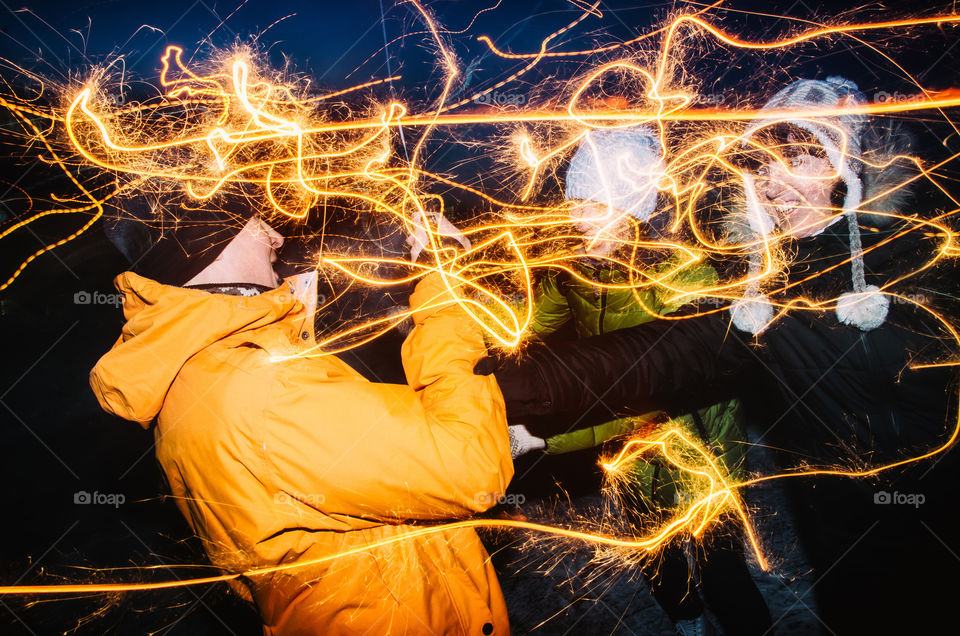 Group of friends of different sexes enjoying out with sparklers trace on city street. Happy people enjoying winter christmas holidays eve with fireworks