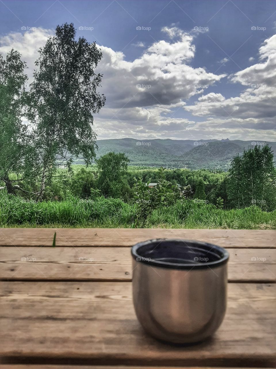кружка от термоса стоит на деревянном столе на улице. на фоне неба и леса