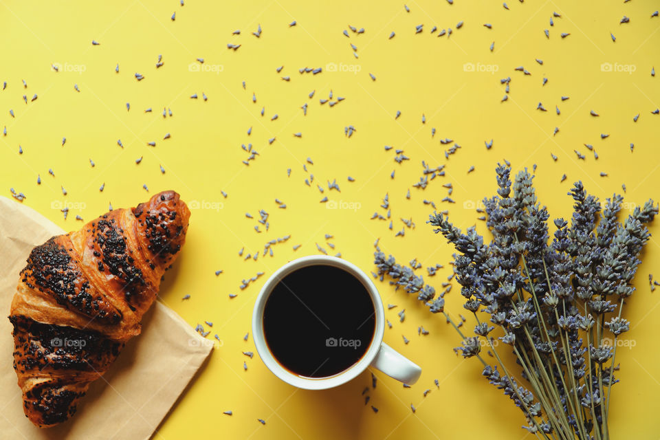 Business working morning with cup of hot coffee, sweet croissant, lavender flowers on yellow background close up. Top view, copy space, flat lay, mockup.