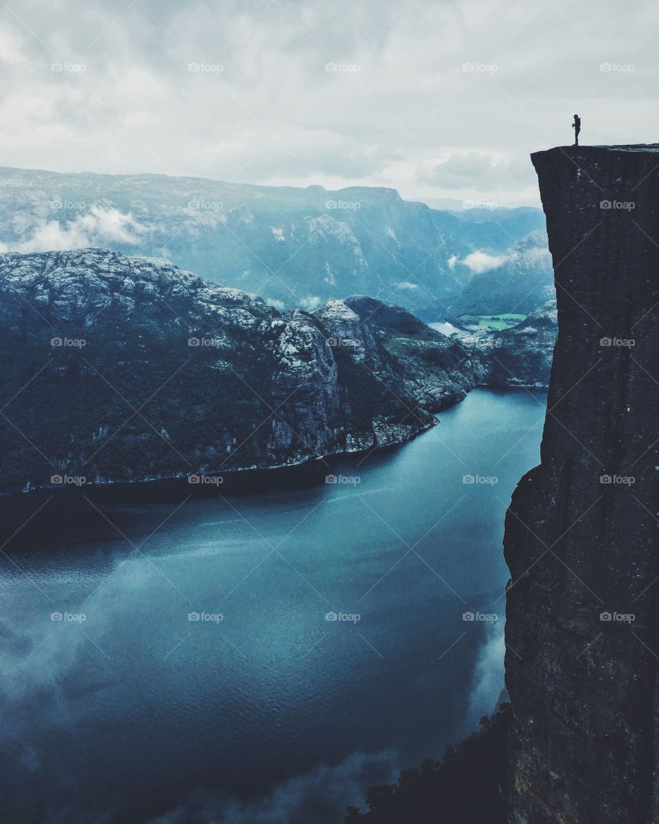 Tiny human standing on the edge of Prekestolen rock in Norway. 