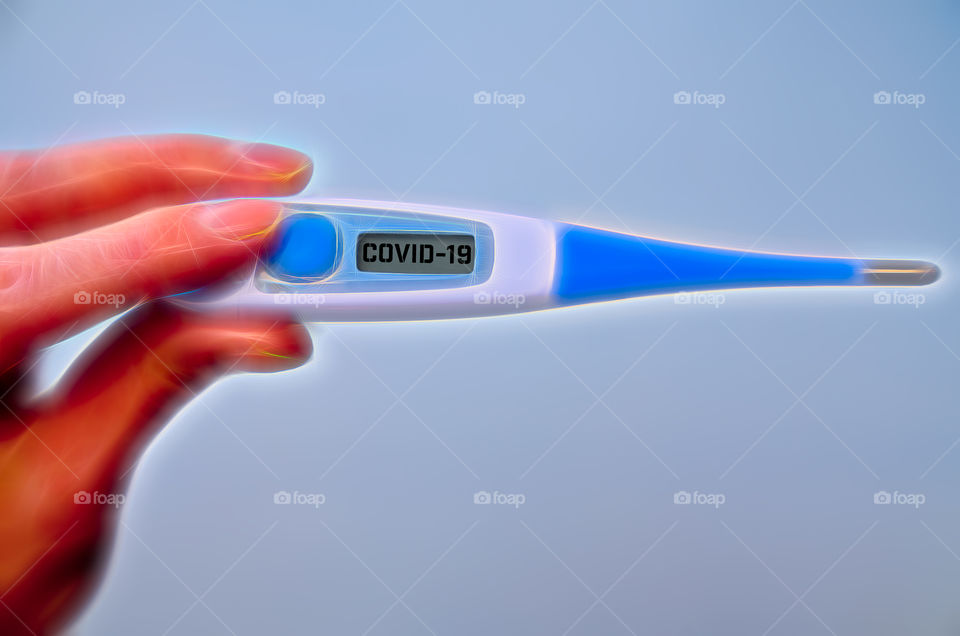 Male hand holds clinical thermometer with covid-19 text on the screen during global covid-19 or corona pandemic.