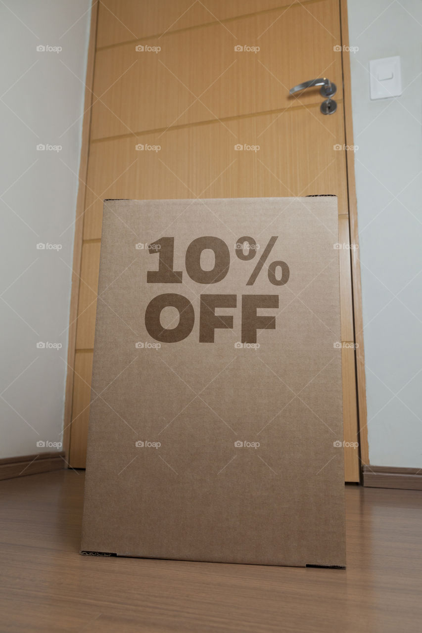 Cardboard box with 10% off order written on the box placed on the floor in an empty room with a neutral background. delivery concept. economy concept. business concept. shopping concept. copy space.