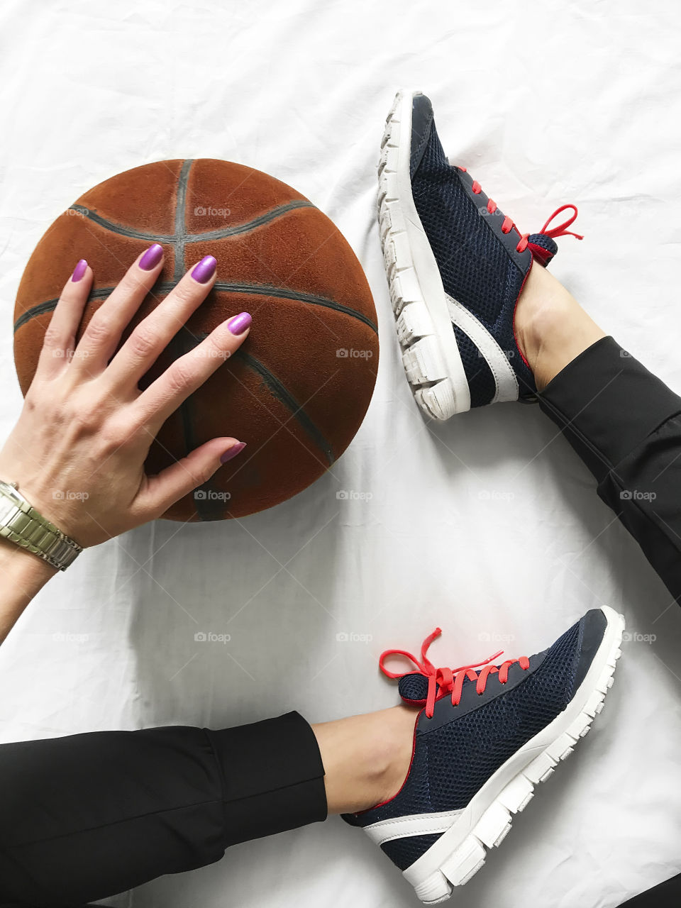 Female hand holding a red Basketball nearby feet wearing female sneakers 