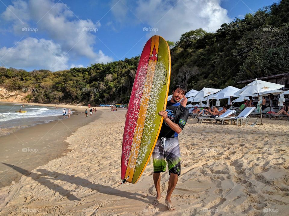 Boy with surfboard on the beach; learn to surf on your next vacation