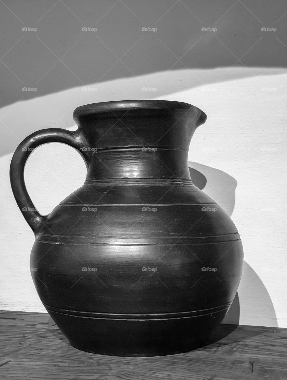 Black and white photo of an ancient clay jug with with shadow on a wooden tabletop