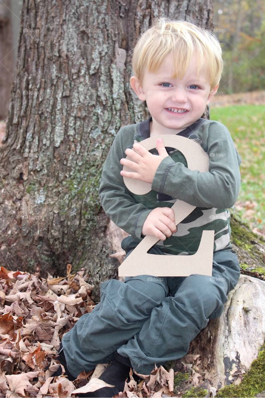 Cute boy sitting near tree trunk in the autumn