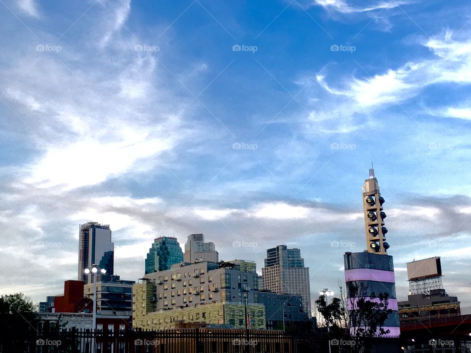 From afar the Long Island City, Queens, New York skyline as seen from beyond Borden Avenue. The sky above shows dramatic cloud patterns. The picture was taken in the Spring of 2019. Hypnotic Productions