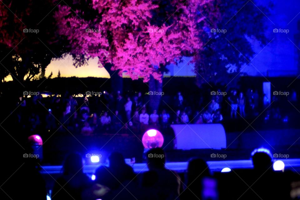Silhouette’s of faceless people in a crowd with bluish purple lighting and illuminated pink tree!
