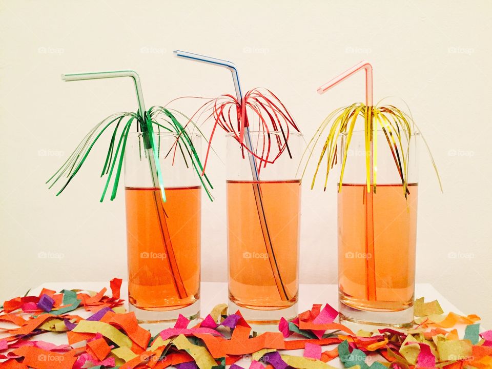 Three cocktails with decorated straws on a table with confetti