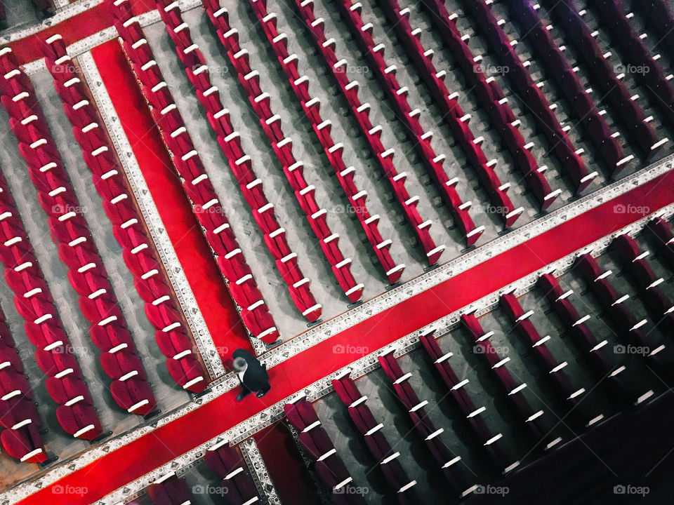 Tiny human walking among the rows of red seats in the theater 