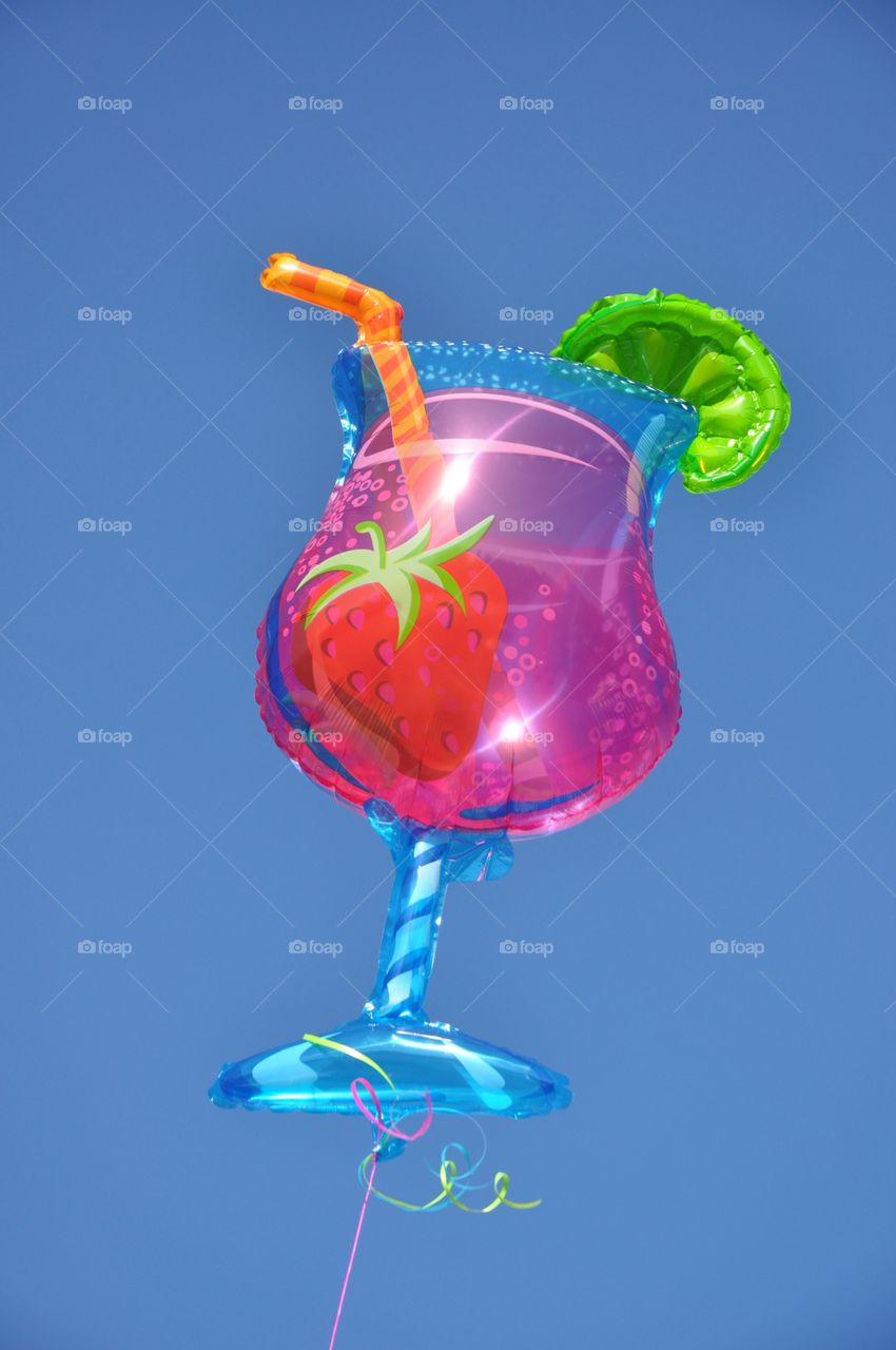 Tropical drink balloon floats against a bright blue sky.