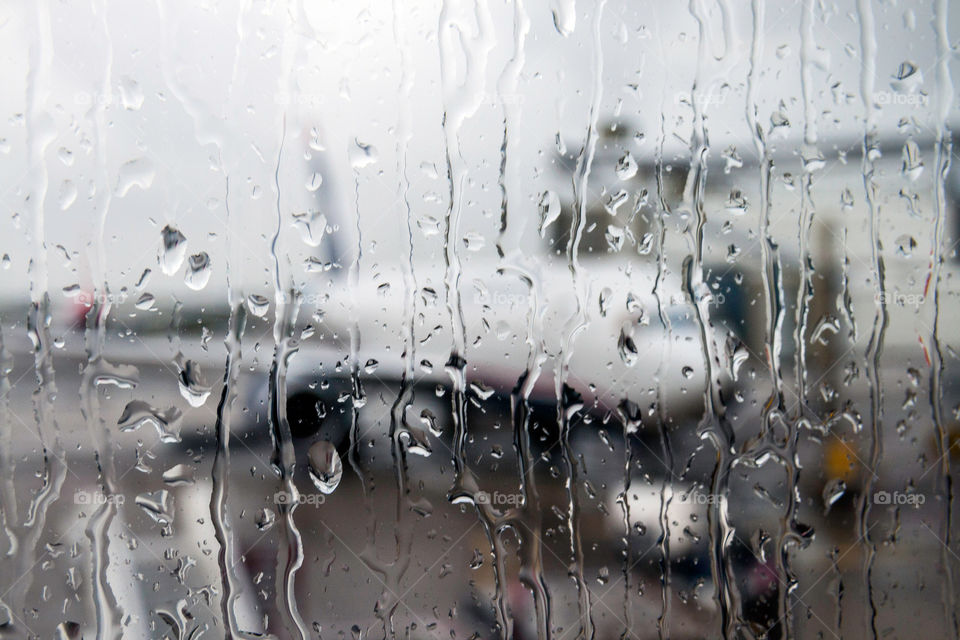 raindrops cascading down the window of an airport terminal while waiting for the plane to depart. 