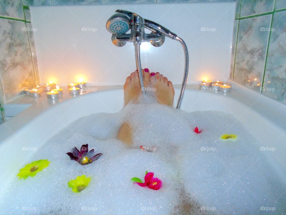 Woman's feet with red nail polish in bubble bath with candles and flowers