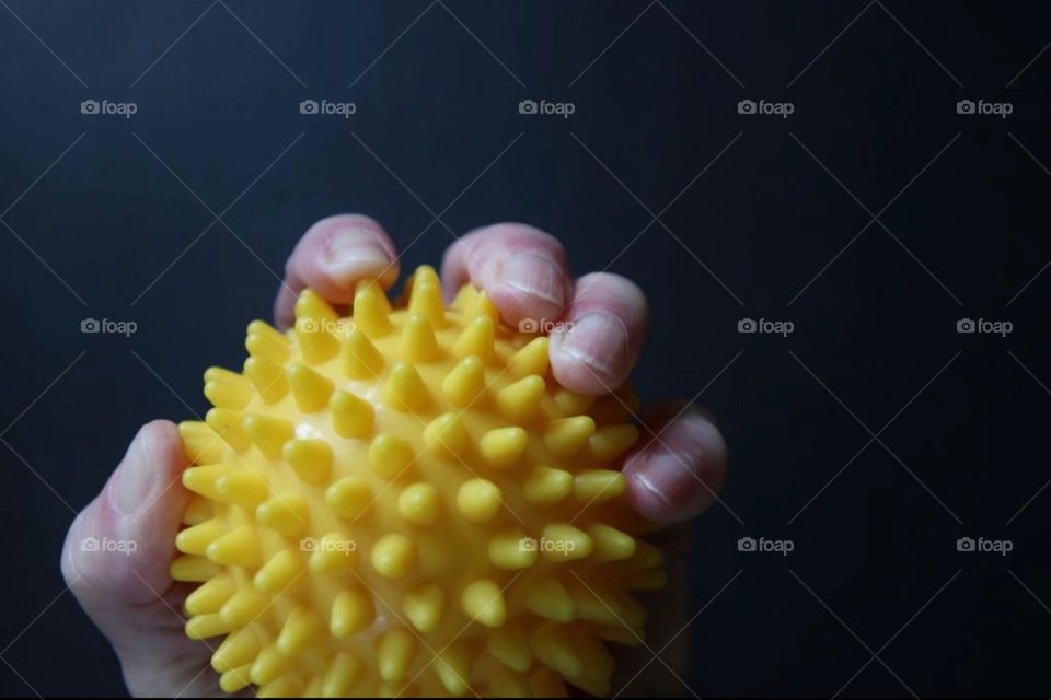 Close-up of a hand grabbing a small yellow exercise ball with studs