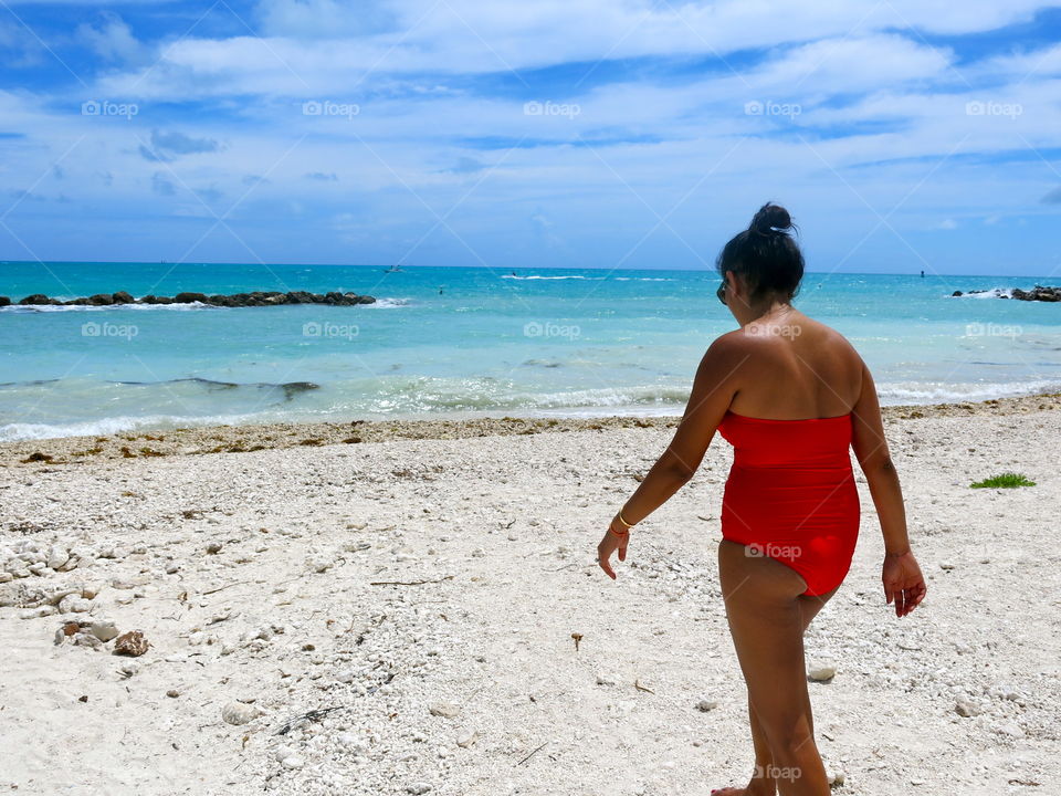 Woman in a red swimsuit walks down to the water at a beautiful beach in key west, FL