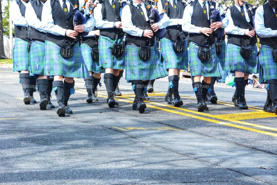 unrecognizable men in Irish kilts marching with bagpipes in a parade