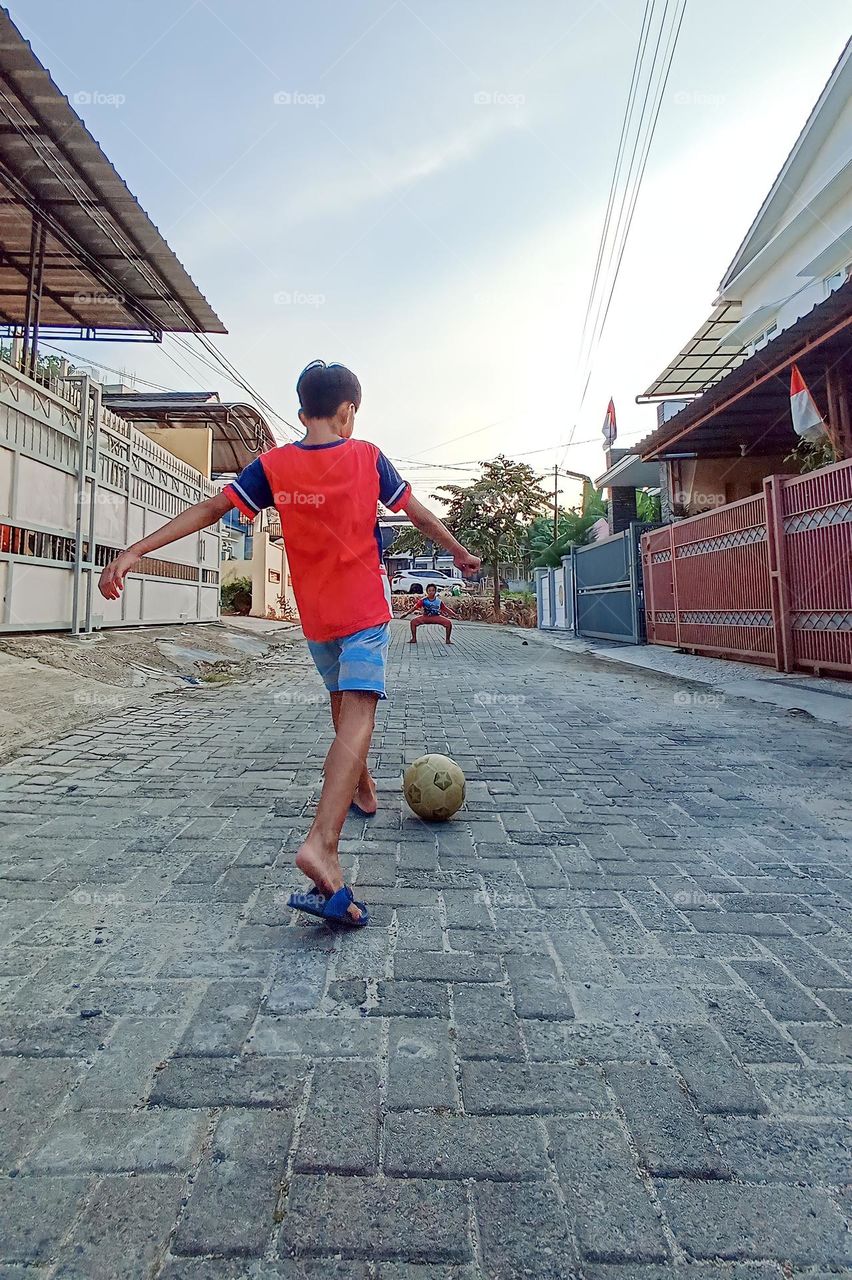 Bandar Lampung, Lampung, Indonesia - December 15, 2023: a child playing ball on a rocky road in a residential area