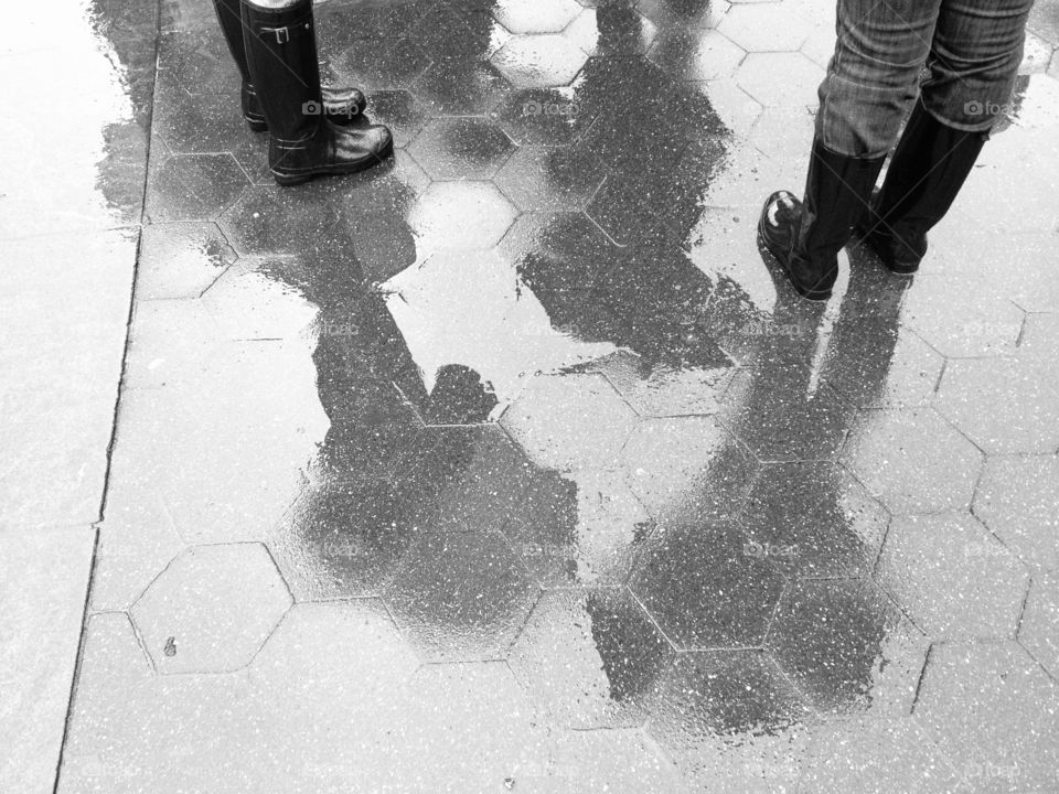 Rain boots and shadows of people holding umbrellas on a rainy day reflected on the wet ground
