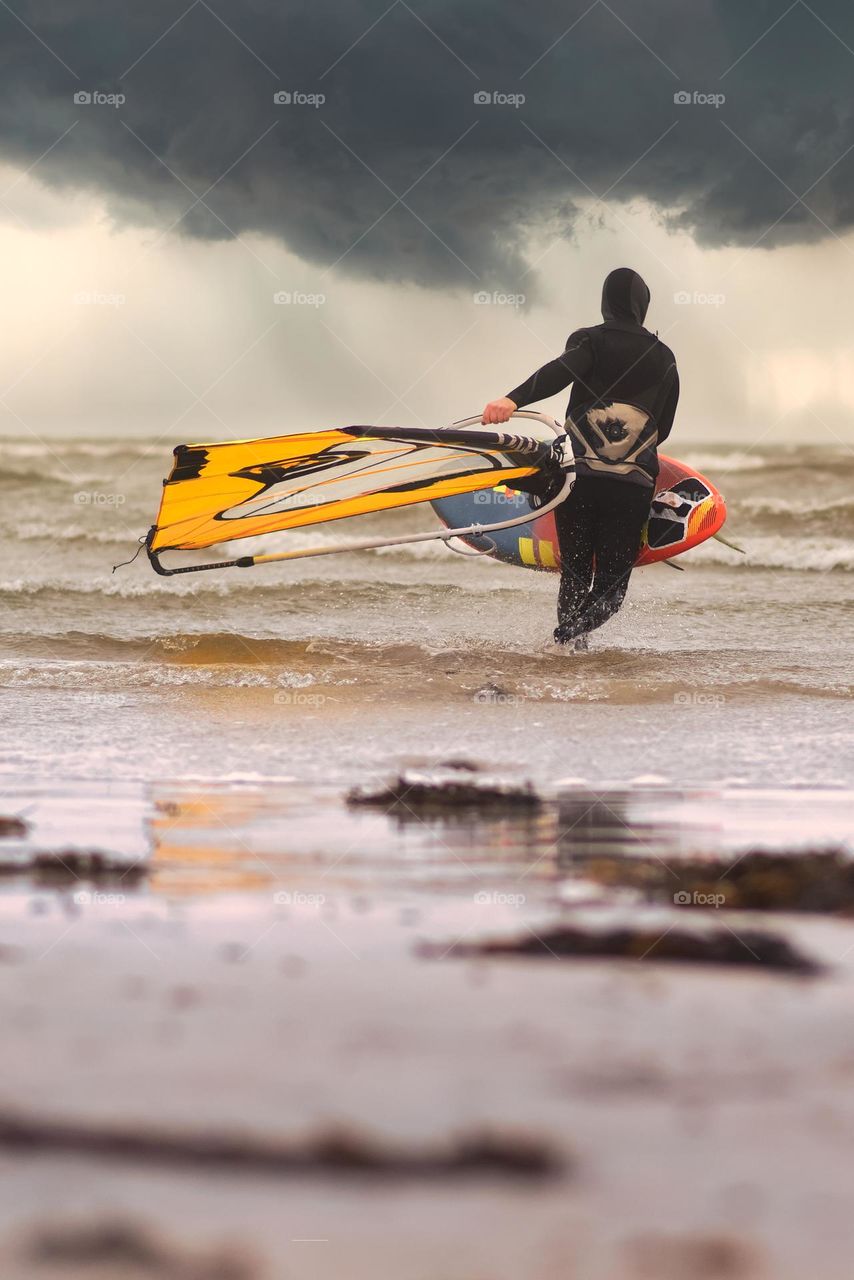 Surfer under dramatic cloudy skies at Silver strand beach in Galway, Ireland