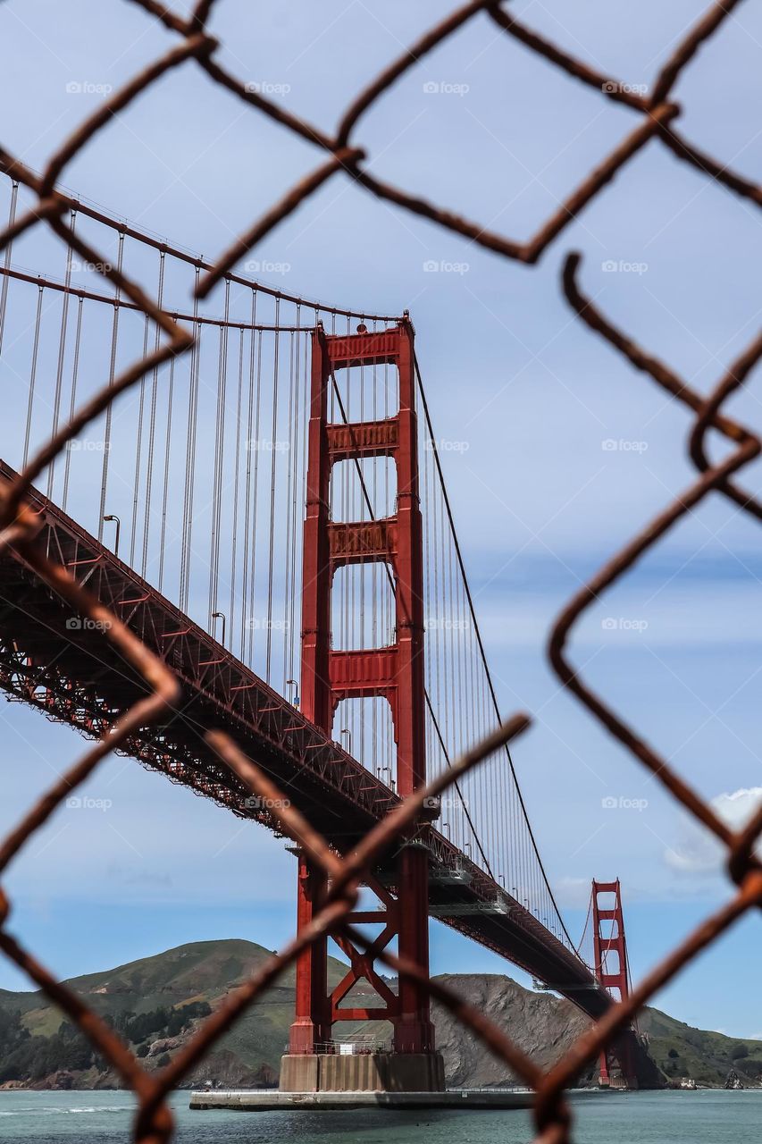 Golden Gate Bridge in San Francisco California seen through a rusty metal wire fence on a clear day still looking majestic at the Fort Point viewing area