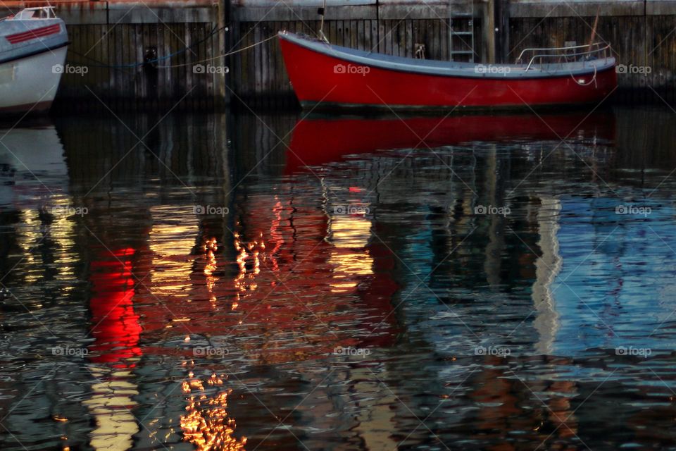 Colorful reflections of illuminated windows in rippled water with boats at night