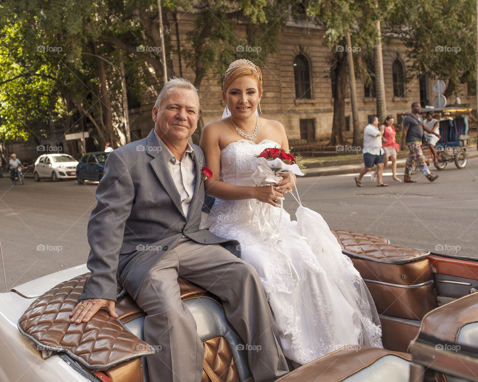 Just married smiling sitting in the old car in the streets of Havana, Cuba
