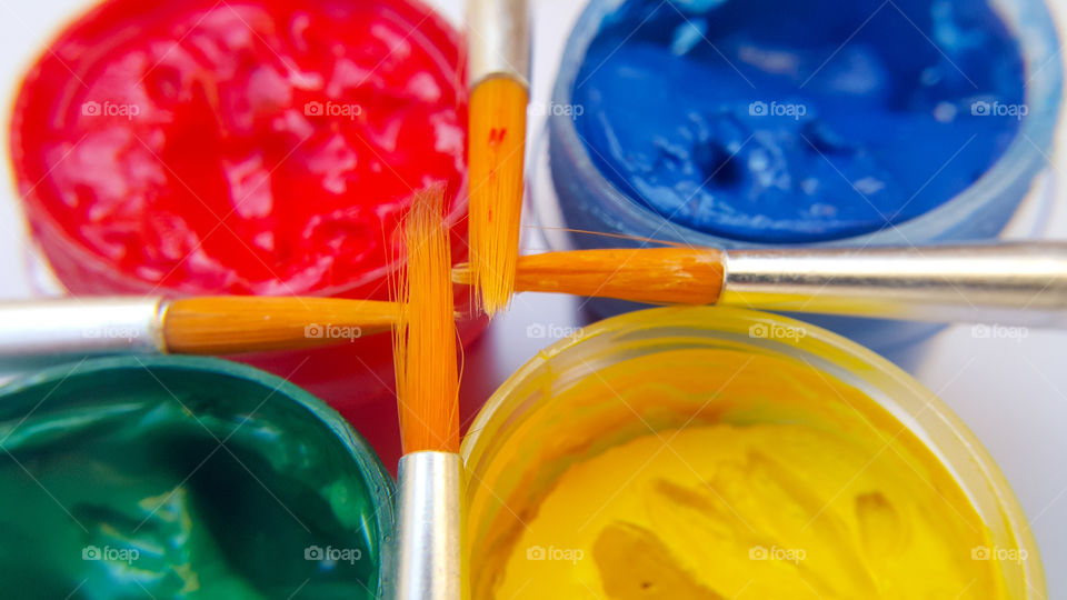 four colors of gouache in open containers, blue, green, red, yellow and four brushes on containers, selective focus and macro photo on two brushes.
